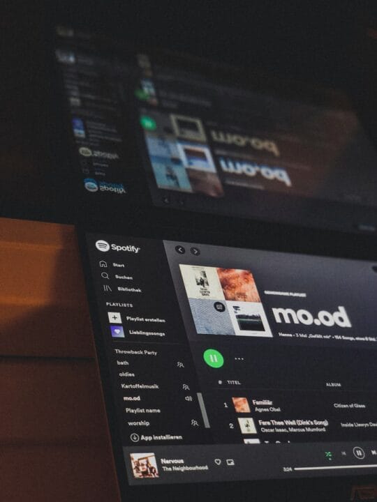 Spotify is open on two laptops displaying music.